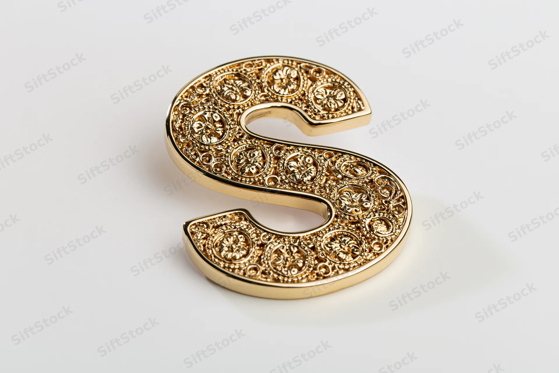 Ornate gold letter s with floral embossing on white surface