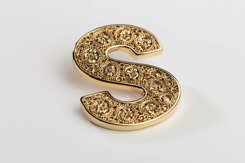 Ornate gold letter s with floral embossing on white surface