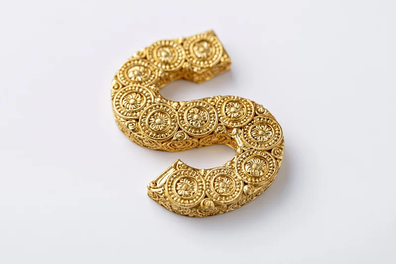 Ornate gold letter s with floral patterns on white background