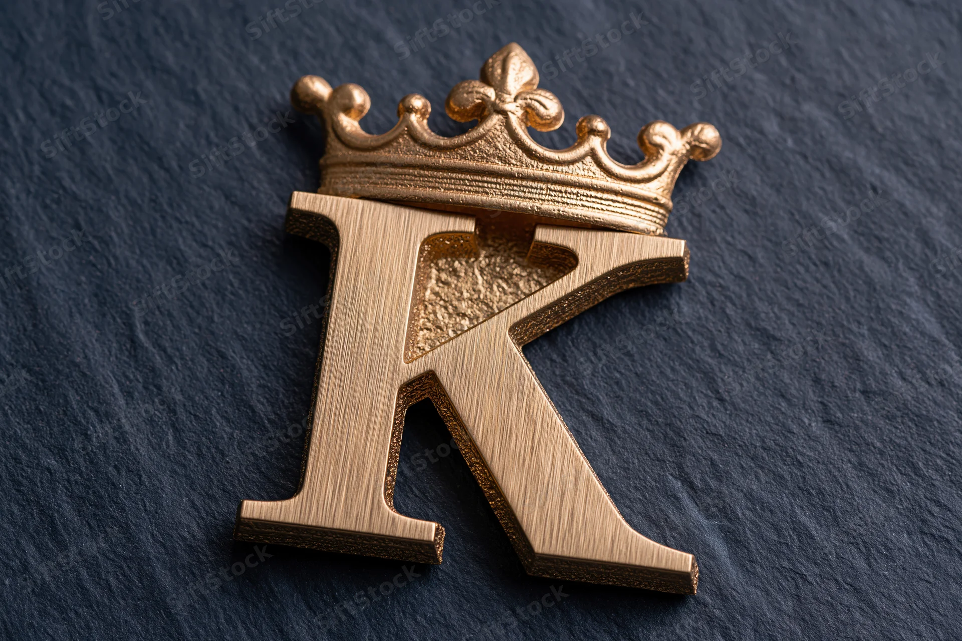 Gold metallic letter k with crown on dark textured surface
