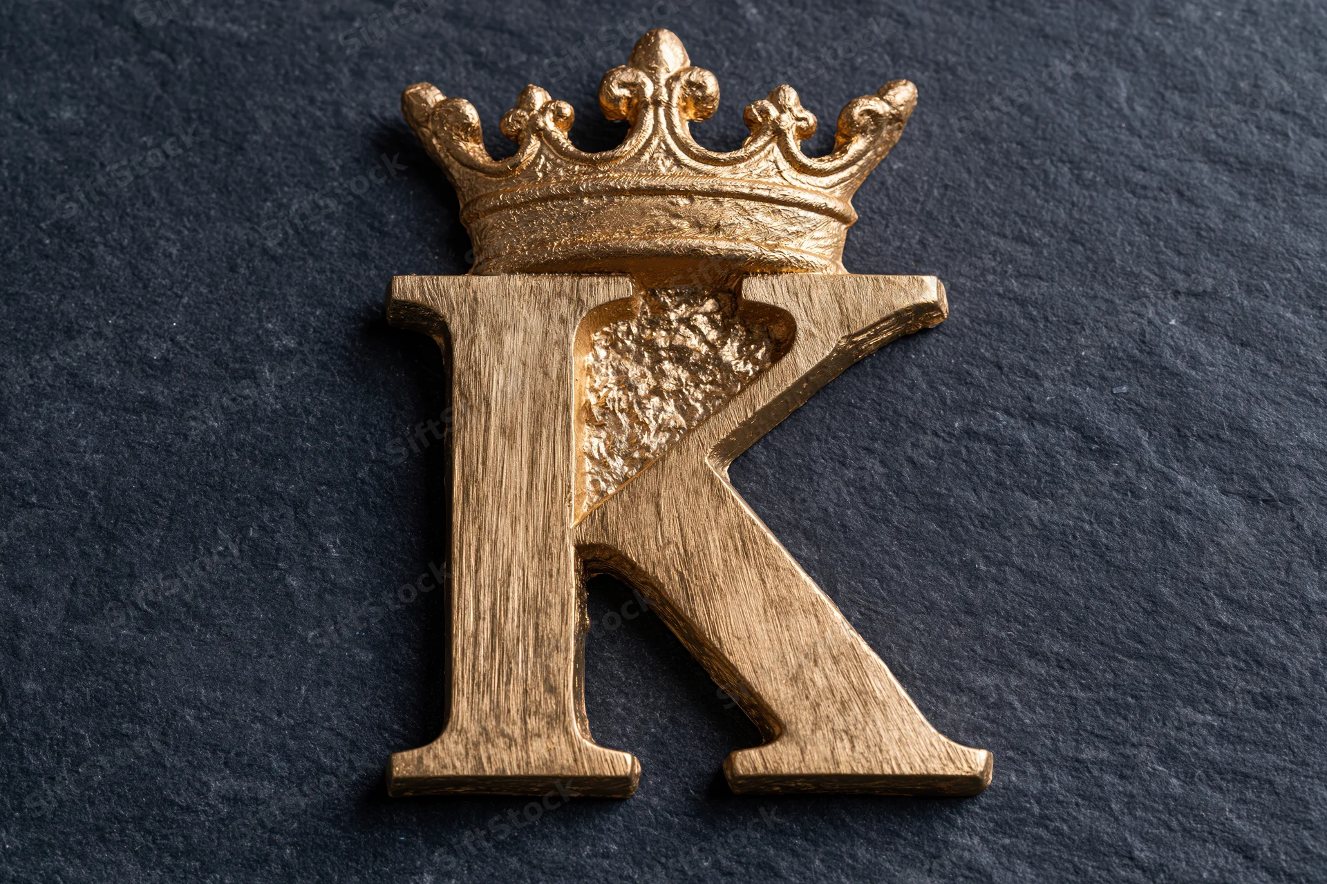 Gold metallic letter k with crown on dark slate surface