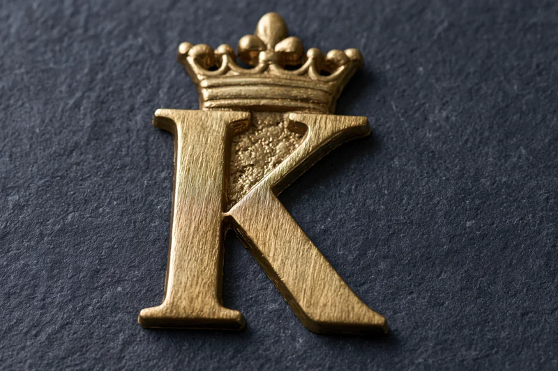 Gold metallic letter k with crown on dark textured surface