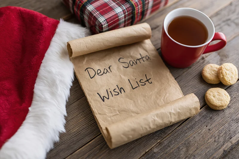 Handwritten santa wish list on kraft paper scroll with cookies and tea on wooden table