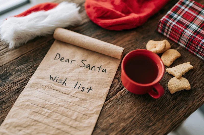Handwritten santa wish list on kraft paper scroll with cookies and milk on wooden table