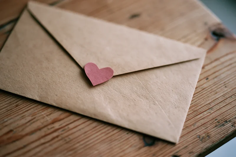 Kraft paper envelope sealed with a red paper heart on a wooden table
