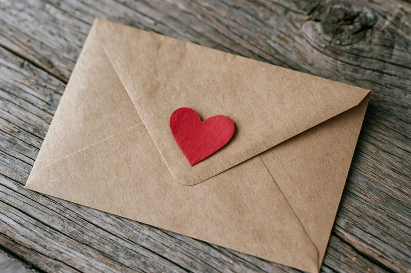 Kraft paper envelope with red heart on wooden surface