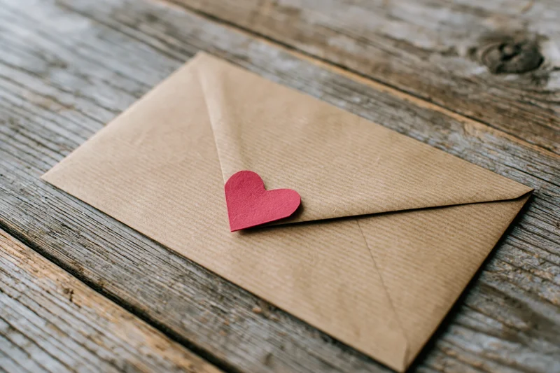 Kraft paper envelope with red paper heart on wooden surface