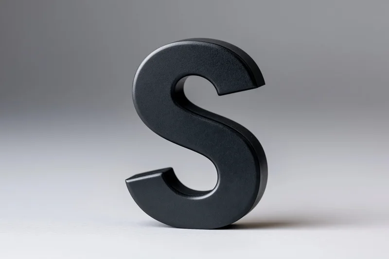 Matte black three-dimensional letter s standing upright on white surface