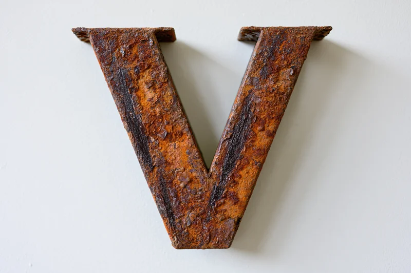 Rusted metal letter v mounted flush against white wall