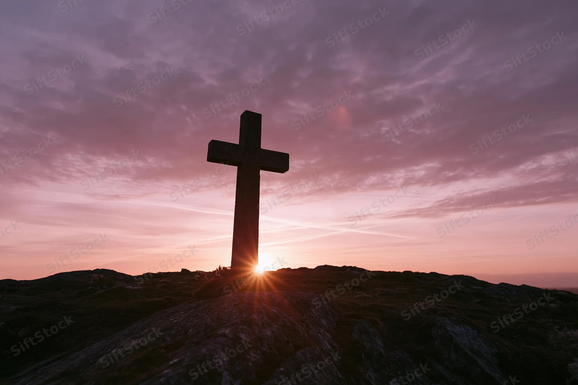 Stone cross silhouetted against a colorful sunset sky on a rocky hilltop