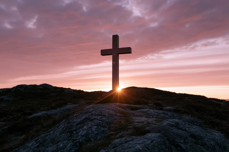 Stone cross silhouetted on rocky hilltop at sunset