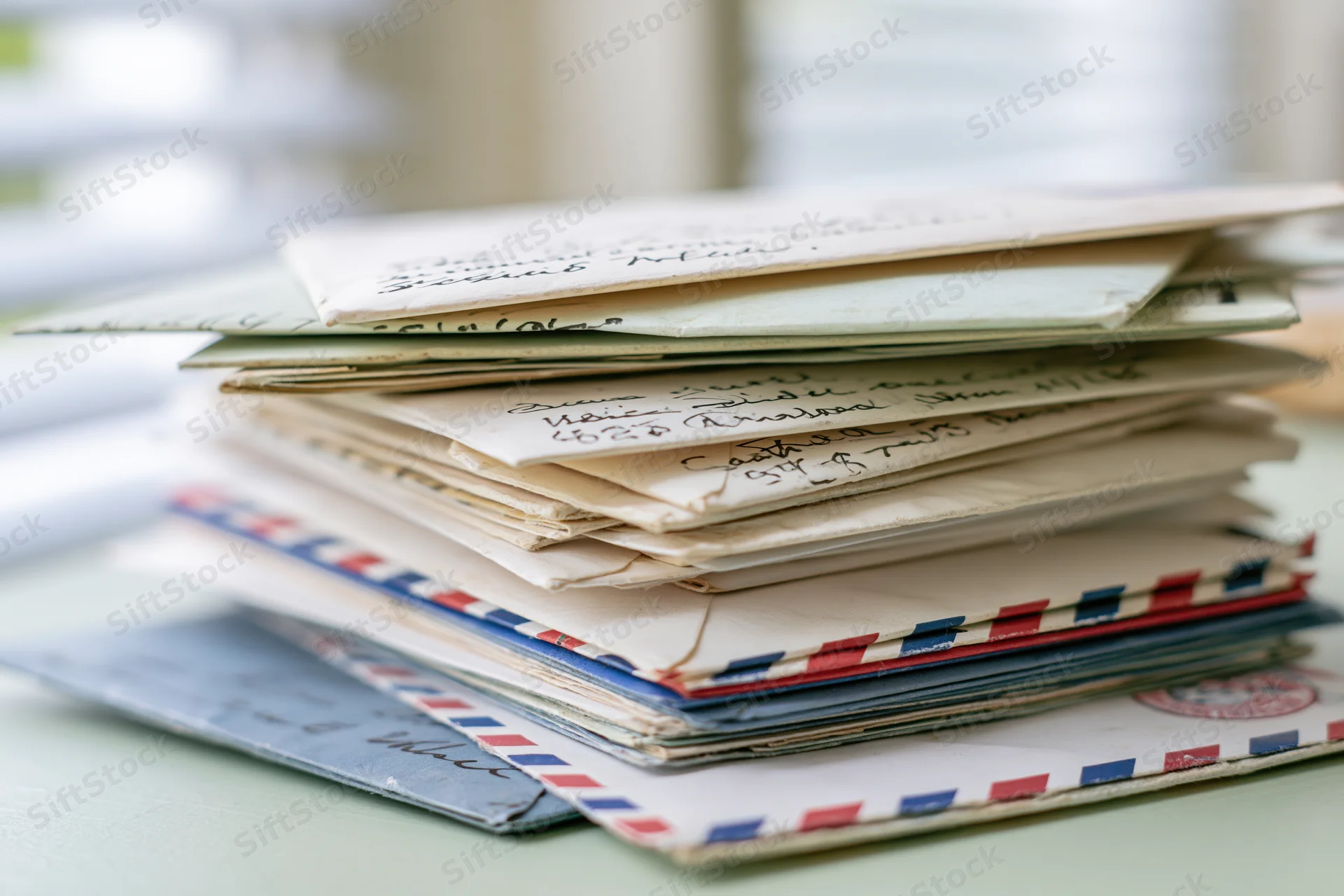 Stack of old handwritten letters and envelopes with airmail stripes on a pale green surface