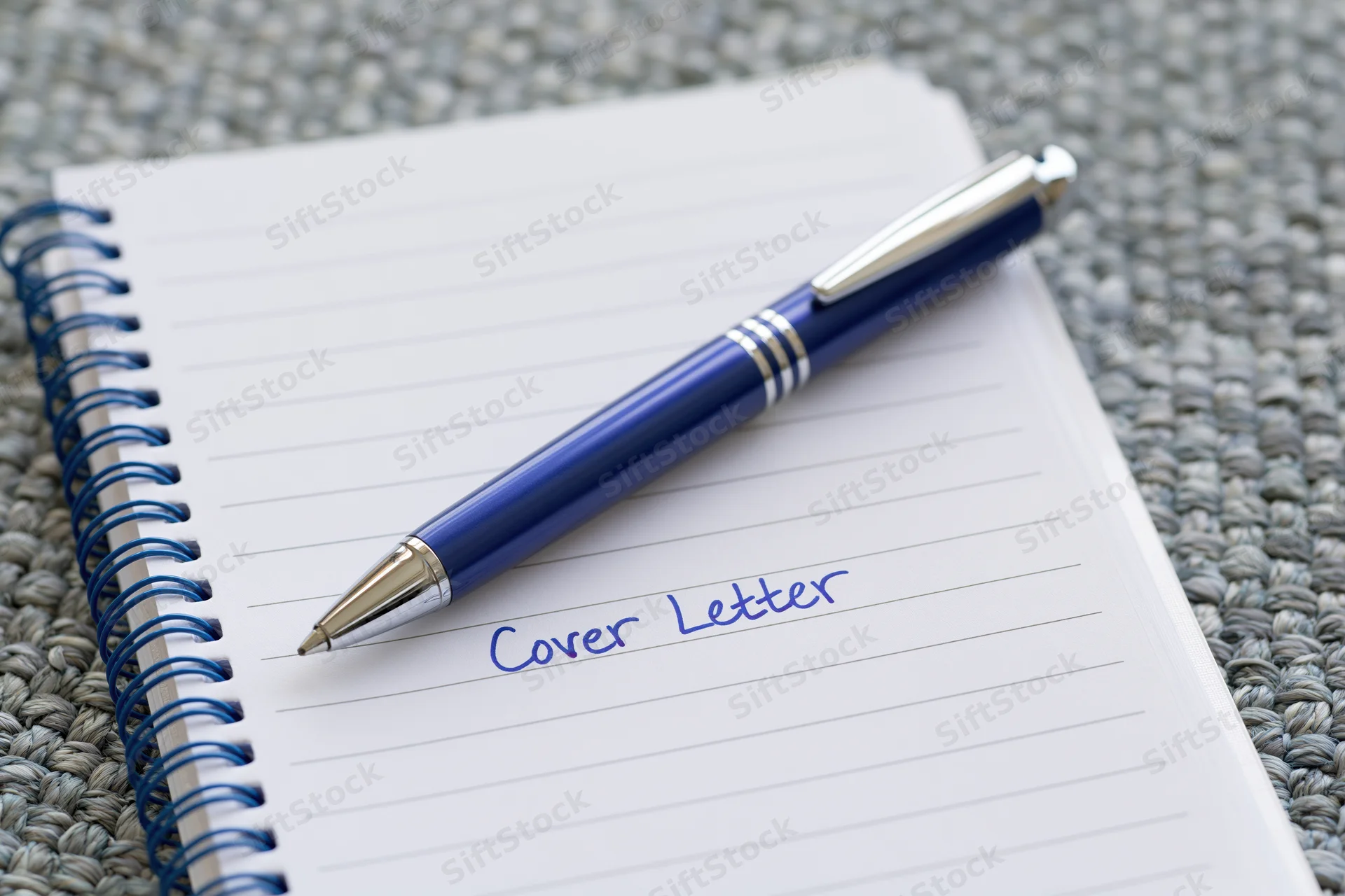 Blue metallic pen resting on open notebook with handwritten cover letter text on lined paper