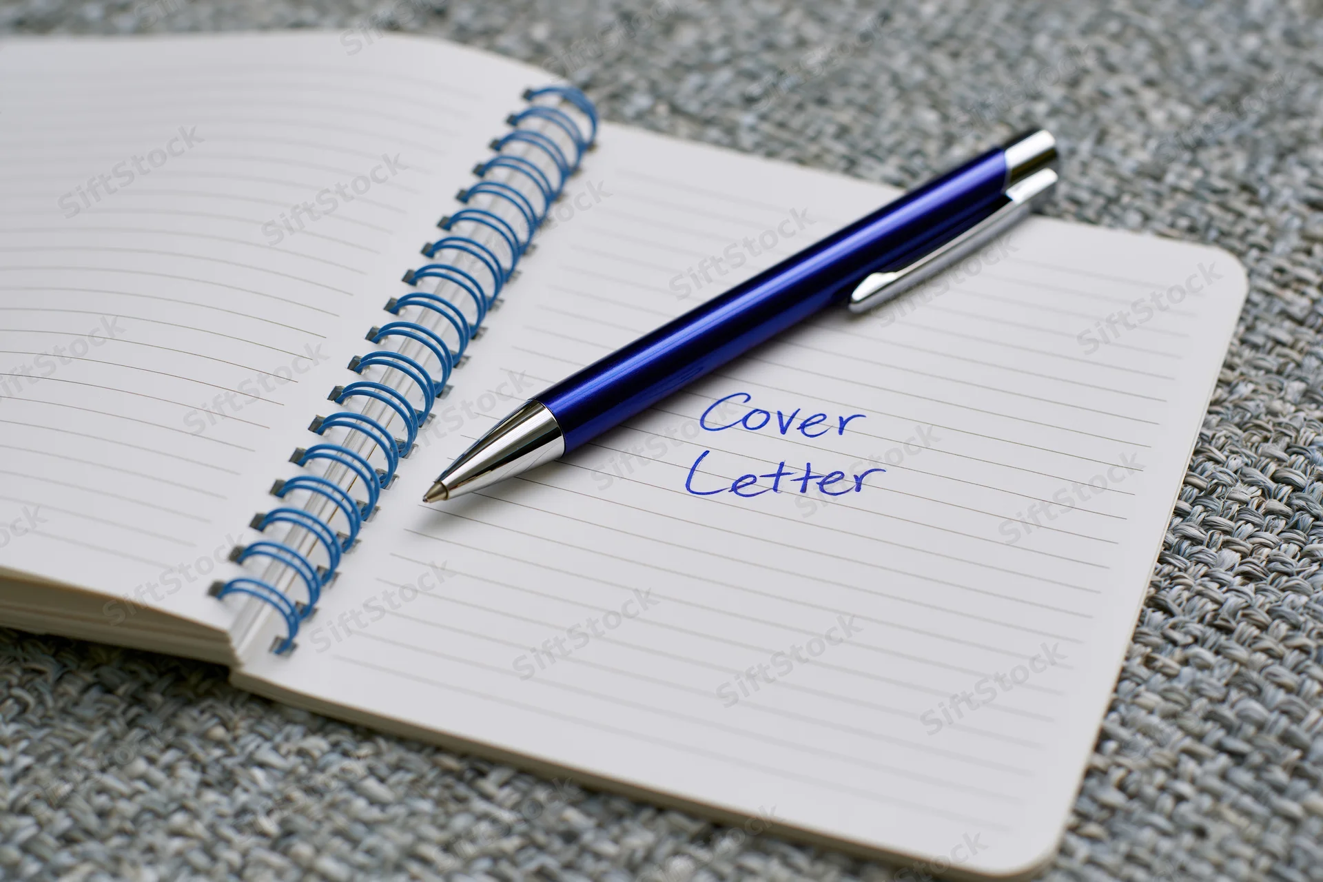 Blue metallic ballpoint pen resting on open spiral notebook with handwritten cover letter text on lined paper