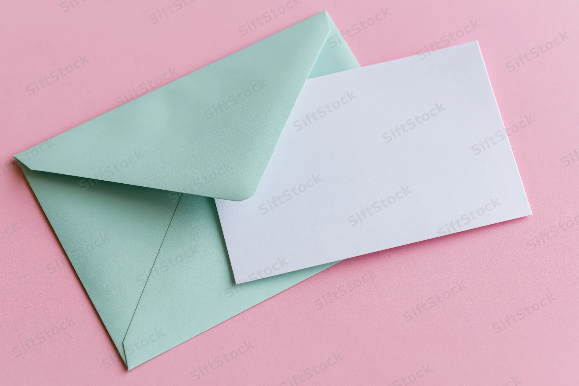Mint green envelope with blank white card on pink surface