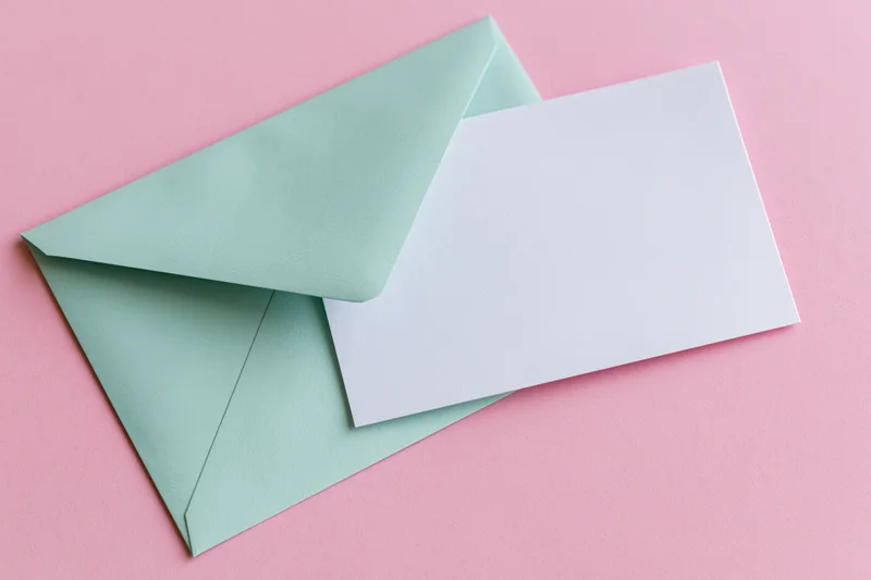 Mint green envelope with blank white card on pink surface