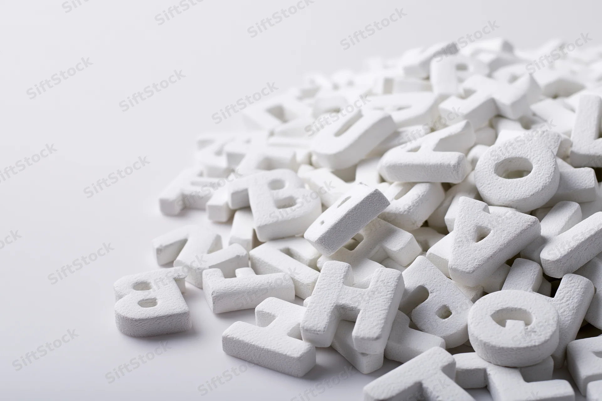 Scattered white foam alphabet letters piled on a plain surface with copyspace