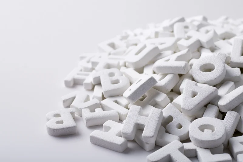 Scattered white foam alphabet letters piled on a plain surface with copyspace