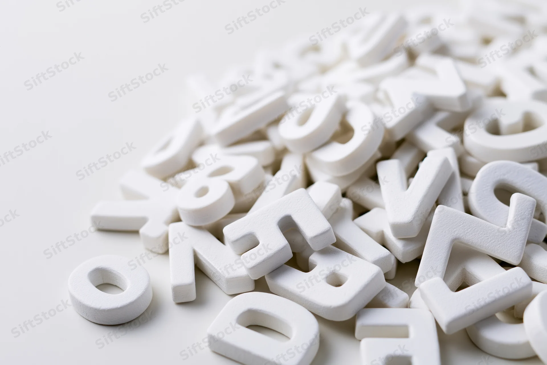 Scattered white foam alphabet letters piled on a plain surface with copyspace