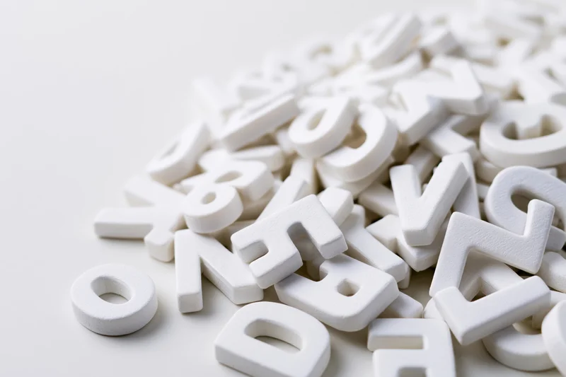 Scattered white foam alphabet letters piled on a plain surface with copyspace