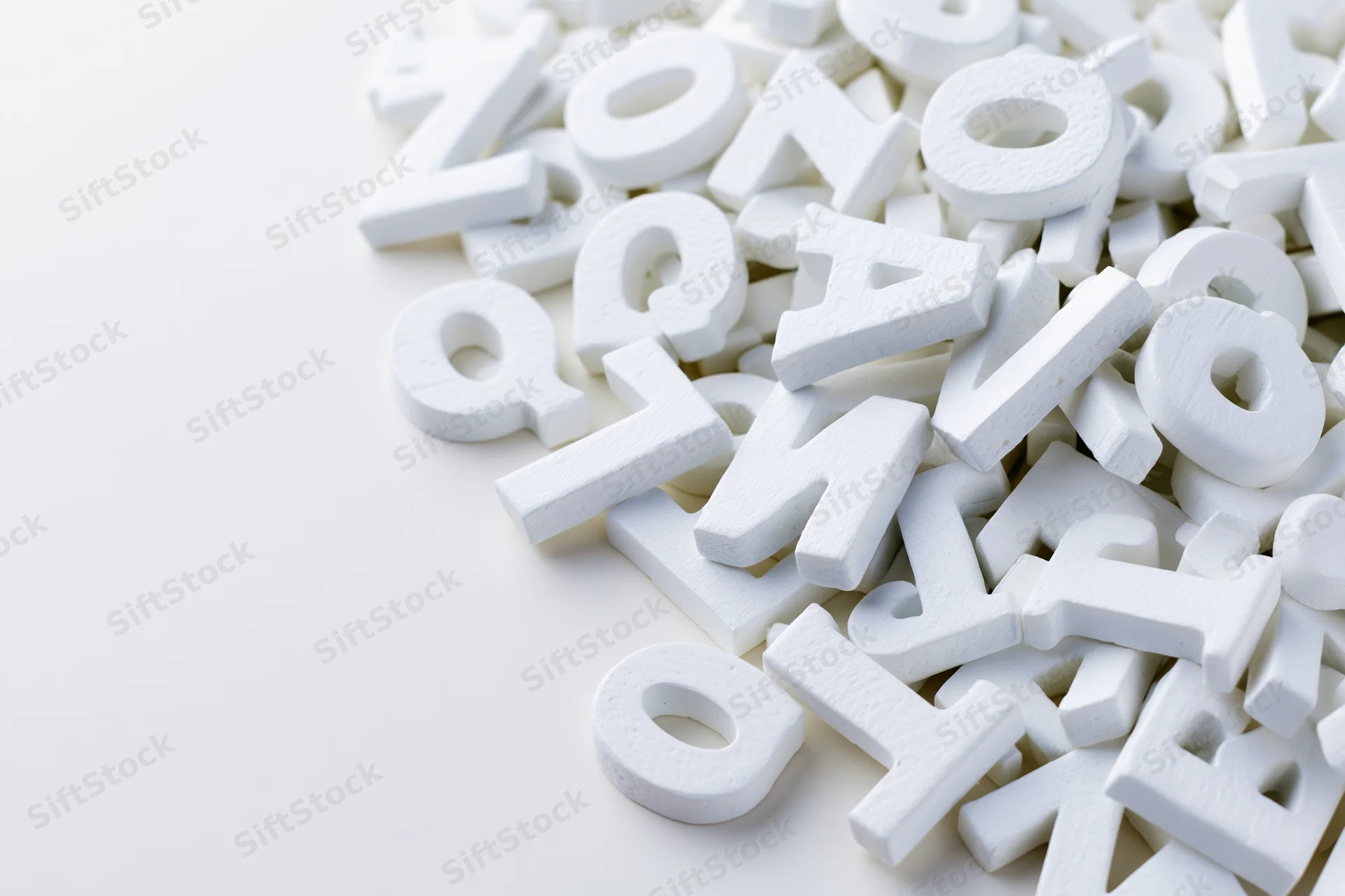 Scattered white foam alphabet letters on a plain white surface with copyspace