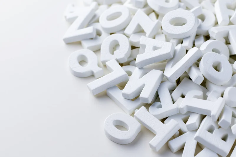 Scattered white foam alphabet letters on a plain white surface with copyspace