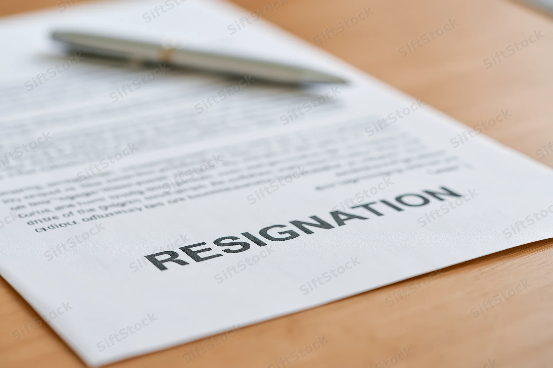 Printed resignation letter on wooden desk with pen resting on top
