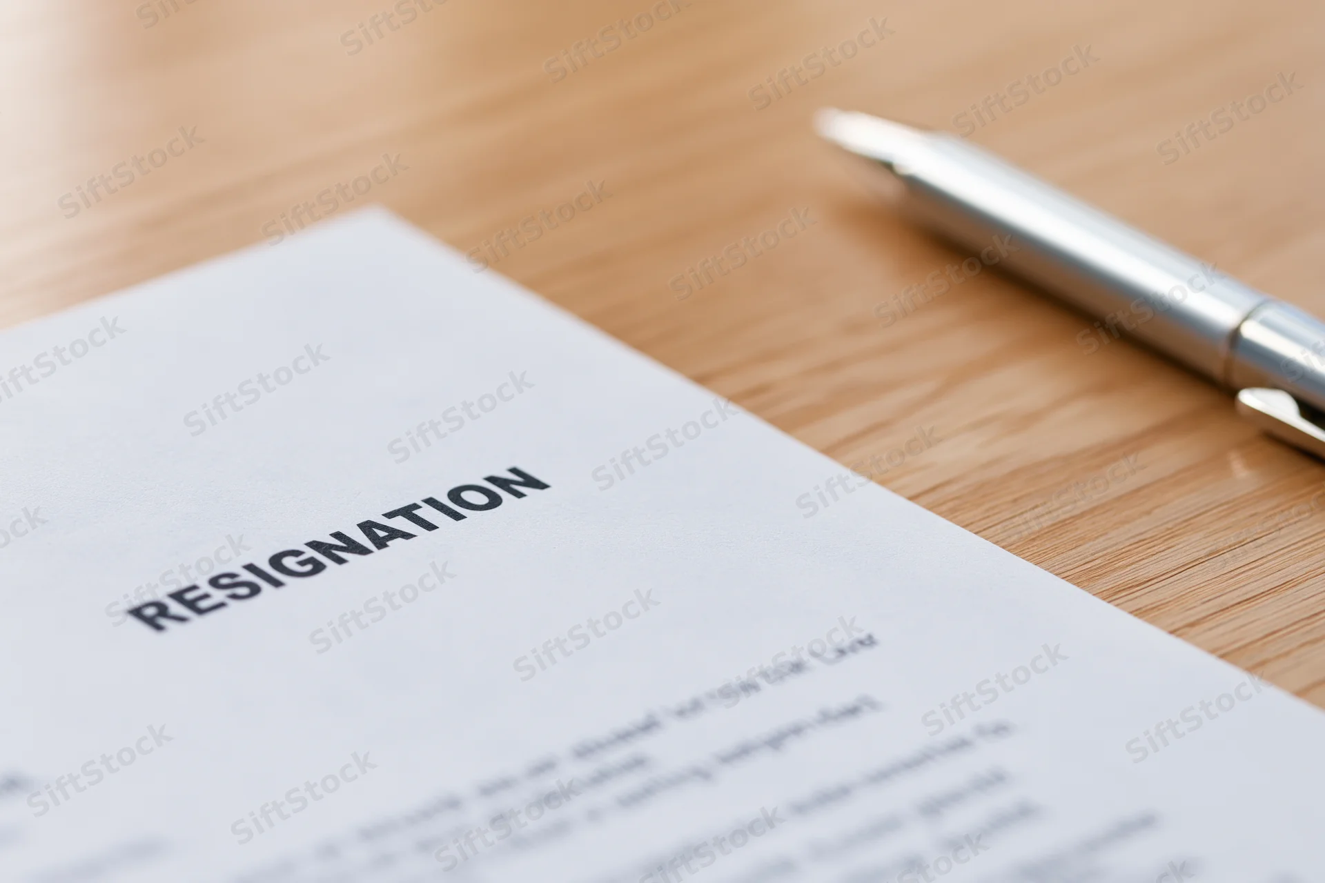 Resignation letter with bold heading on wooden desk beside a silver pen