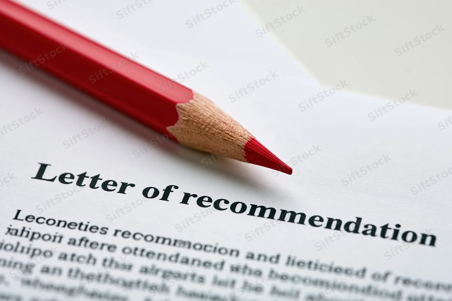 Red pencil resting diagonally on printed letter of recommendation document