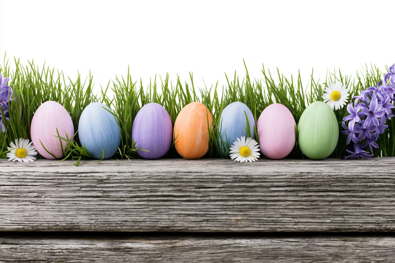 Colorful painted easter eggs nestled in fresh green grass with flowers on wooden plank