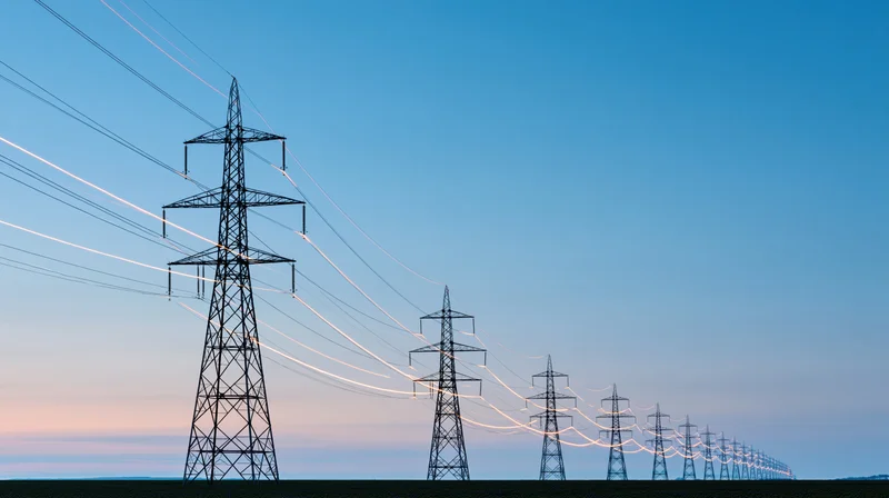 Row of high-voltage steel transmission towers receding into the distance under a twilight sky