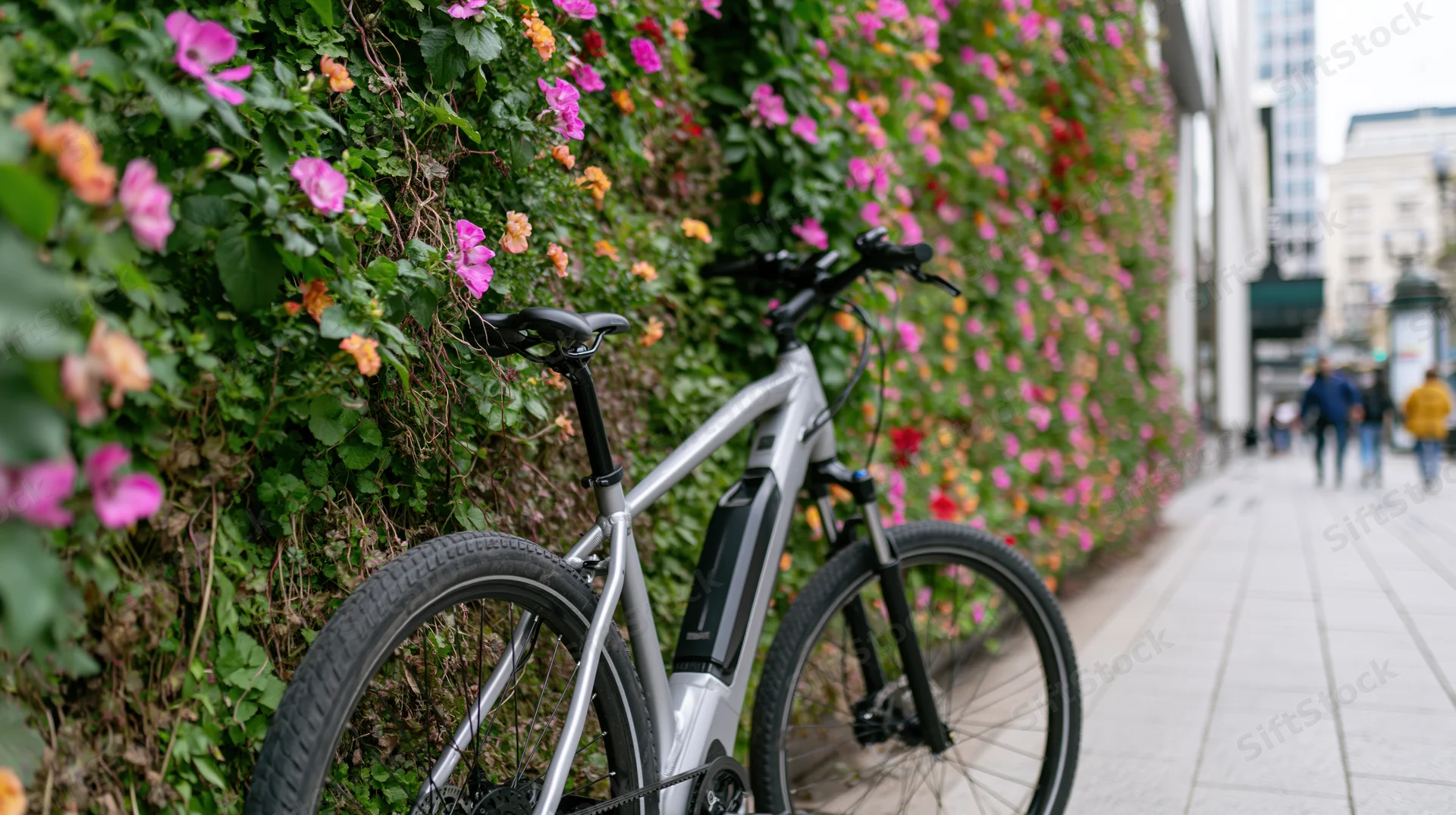 Silver electric bicycle parked on city sidewalk beside flowering green wall