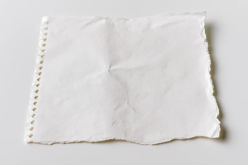 Torn blank notebook page with spiral binding lying flat on white surface