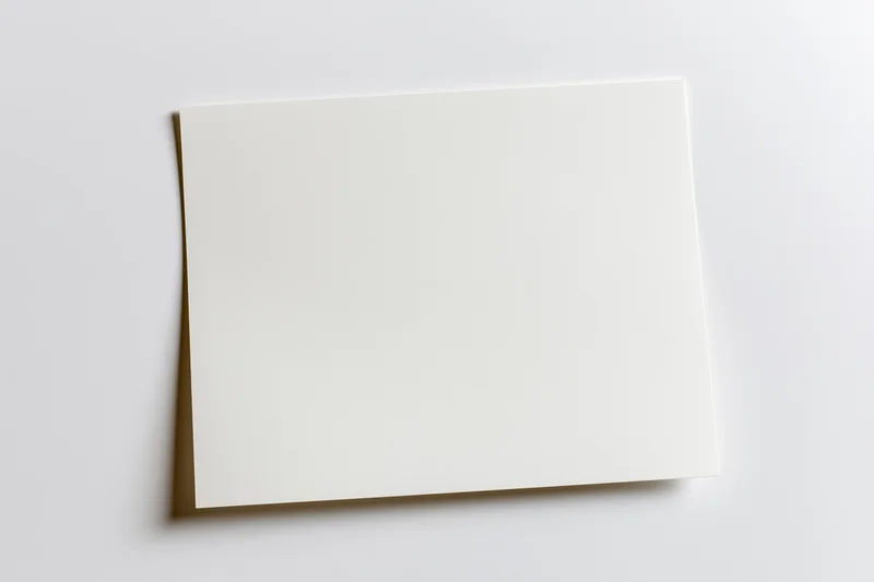 Blank white paper sheet lying flat on a light surface viewed from above