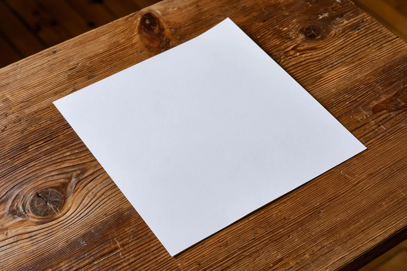 Blank white paper sheet lying flat on rustic wooden table surface