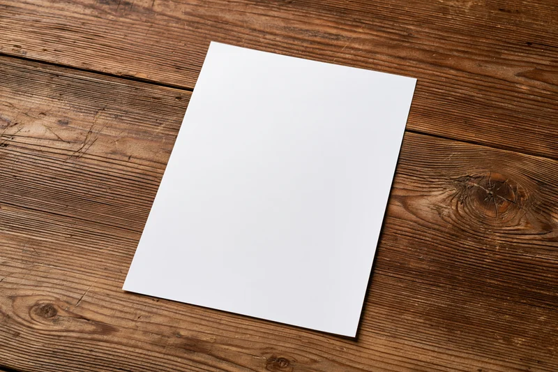 Blank white paper sheet lying flat on rustic wooden table surface