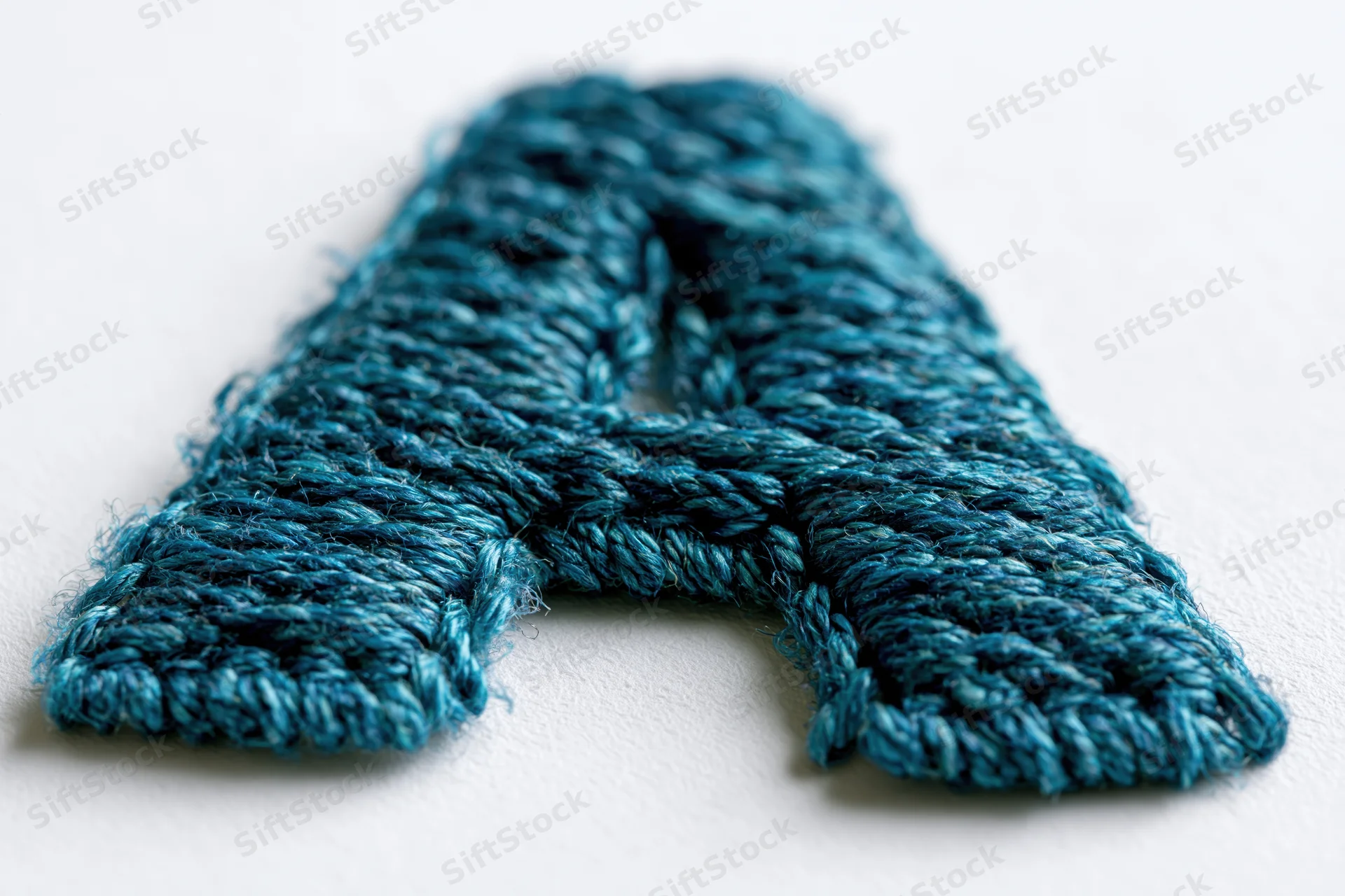 Embroidered letter a made of blue thread on white surface