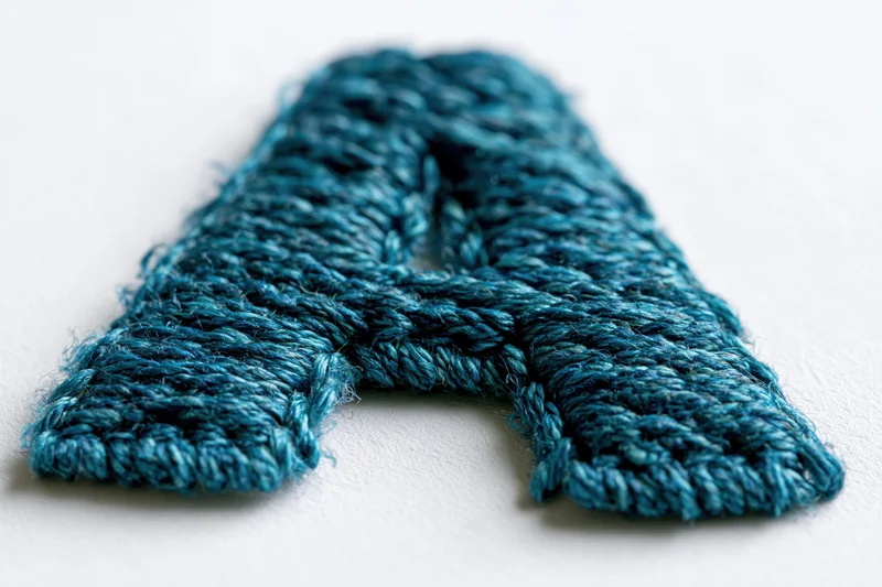 Embroidered letter a made of blue thread on white surface