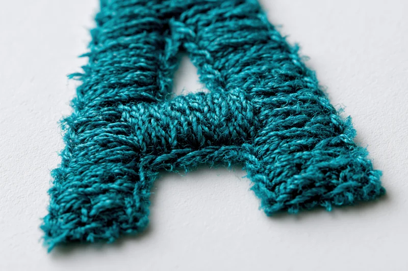 Embroidered letter a made of teal thread on white background