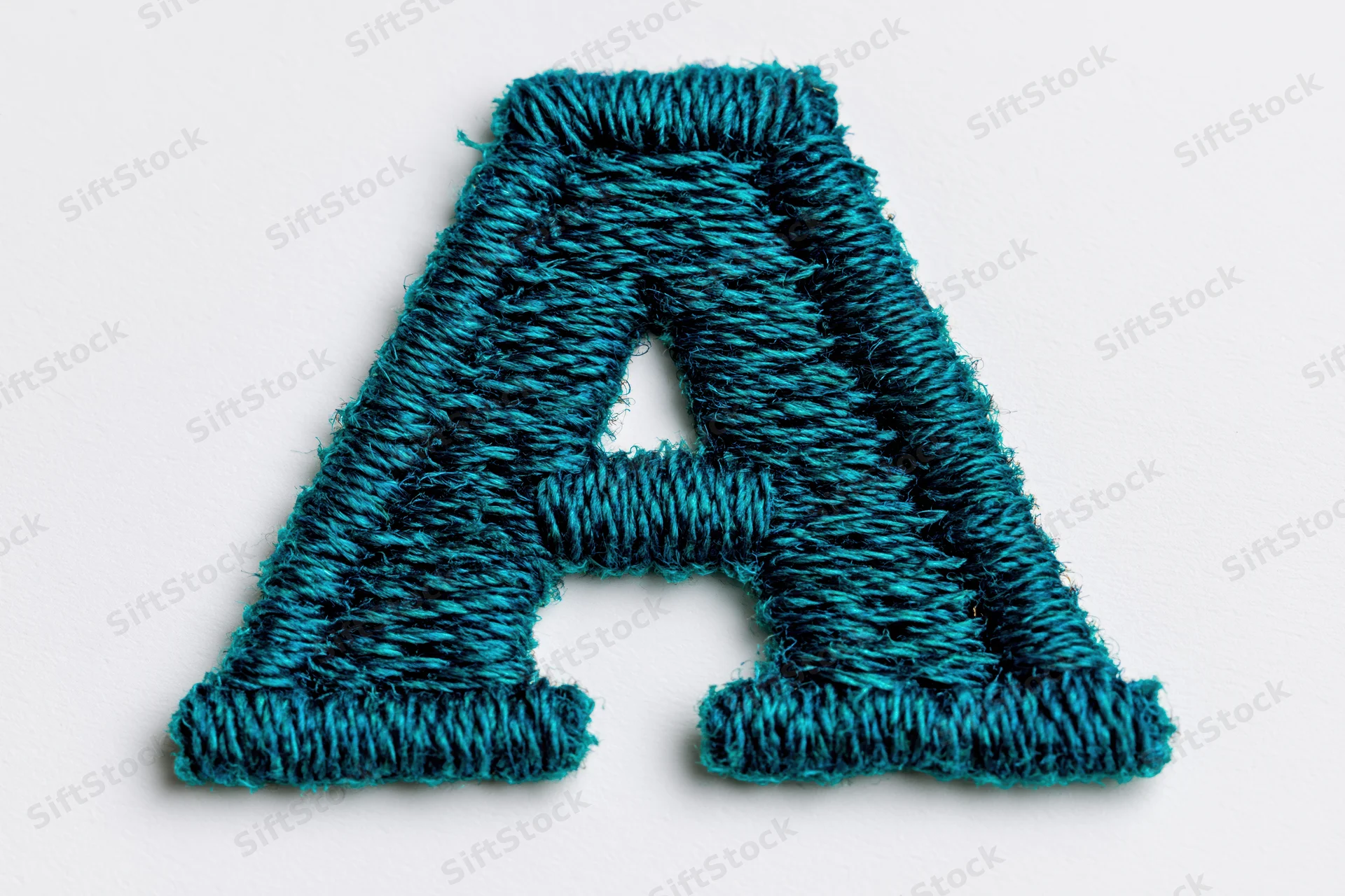 Embroidered letter a made of teal thread on white background