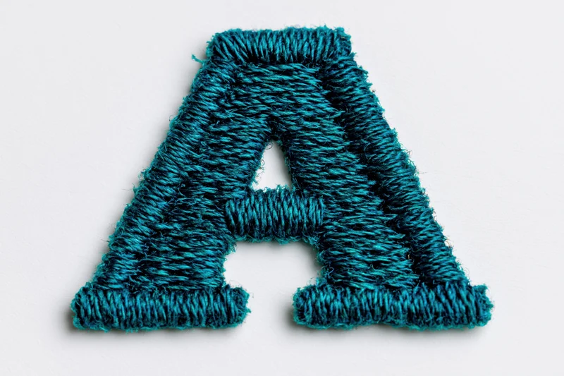 Embroidered letter a made of teal thread on white background