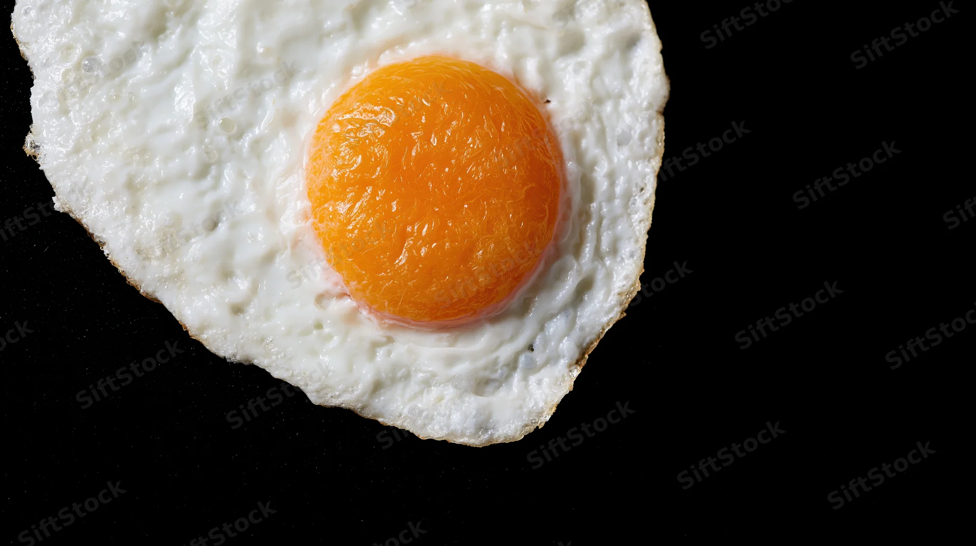Fried egg sunny-side-up on black surface with copyspace to the right