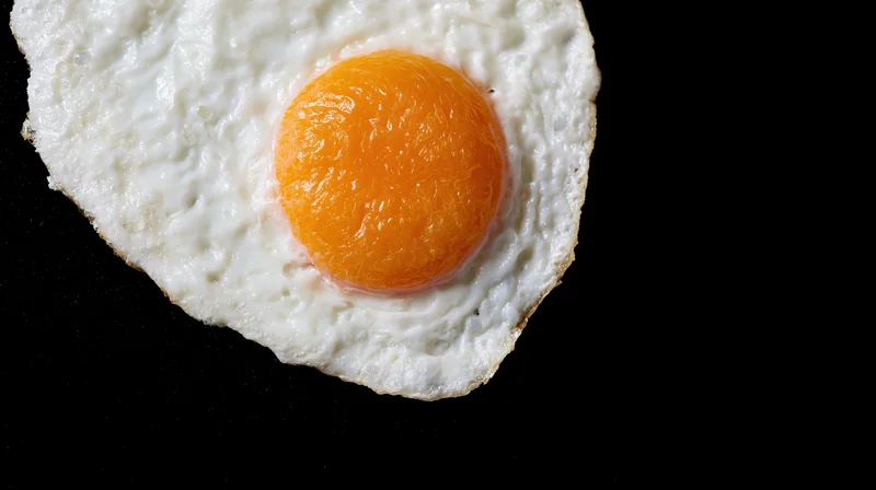 Fried egg sunny-side-up on black surface with copyspace to the right