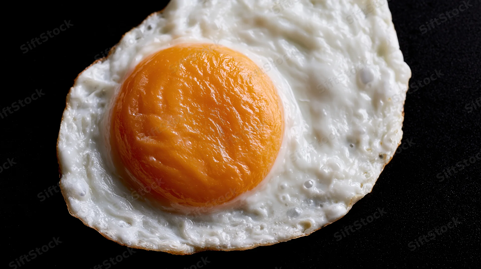 Fried egg sunny-side-up on black surface viewed from above