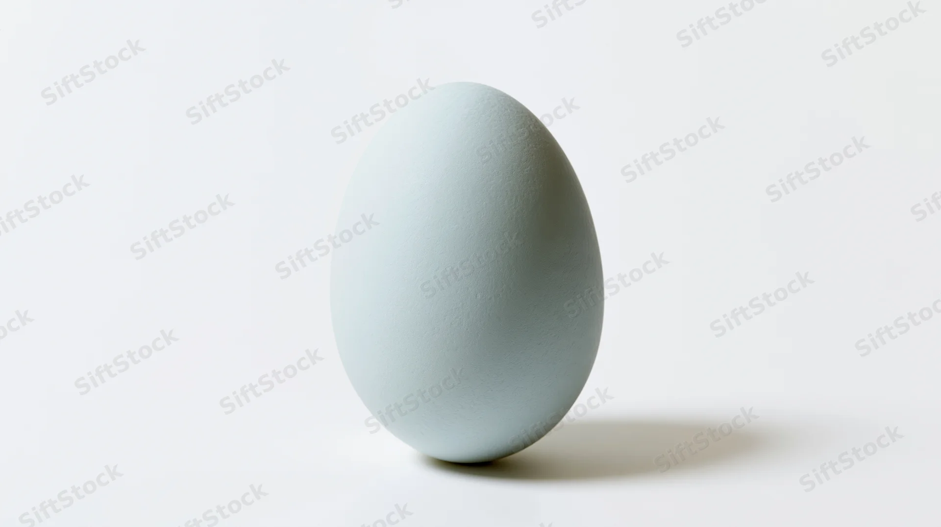 Pale blue egg standing upright on white surface with soft shadow