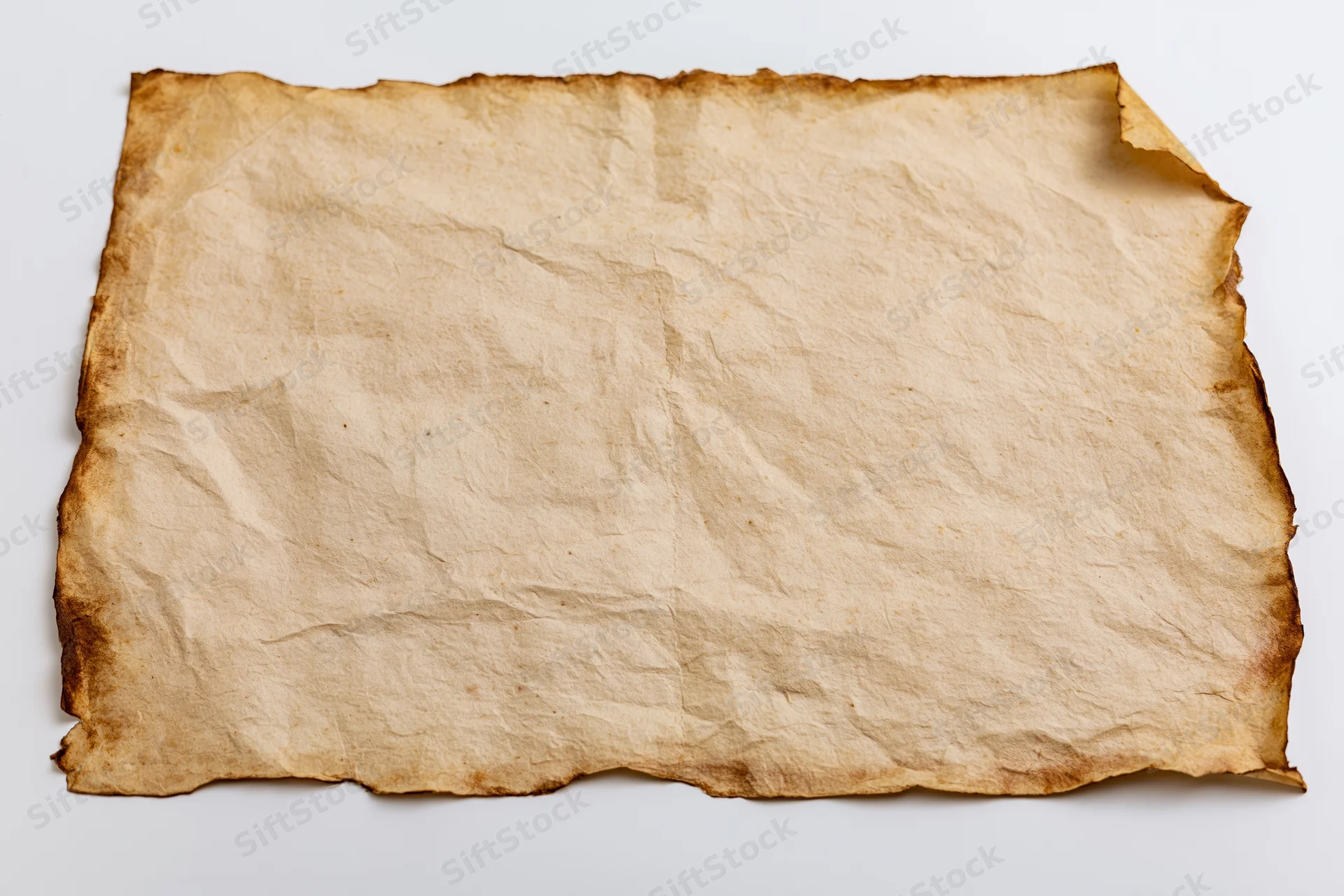 Aged yellowed paper sheet lying flat on white surface with crumpled texture and burnt edges