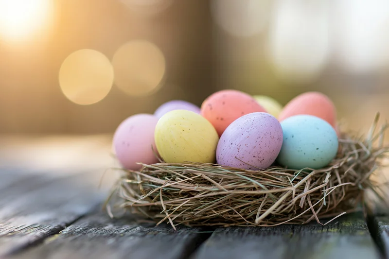 Pastel-painted easter eggs in a straw nest on a wooden table with warm bokeh background