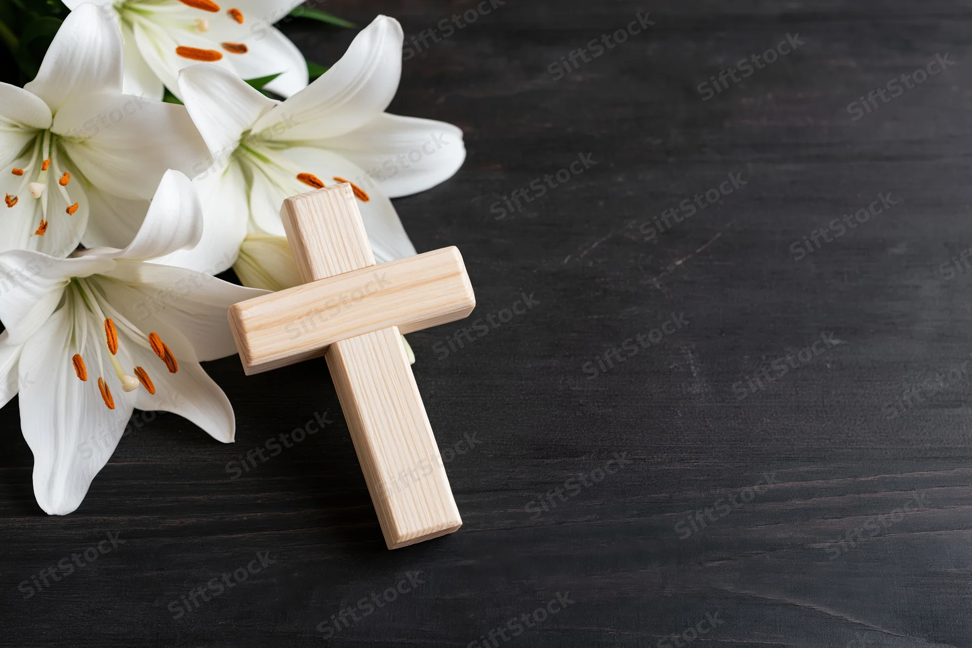 Wooden cross leaning against white lilies on dark wooden surface