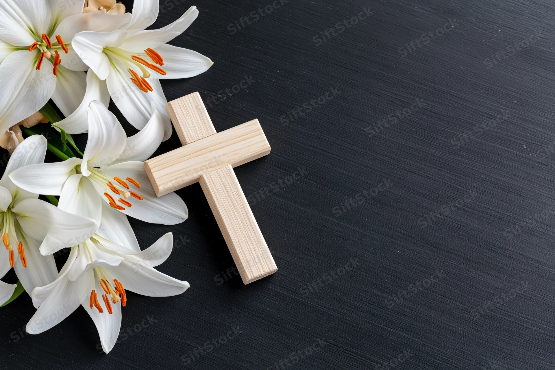 Wooden cross and white lilies arranged on dark surface with copyspace