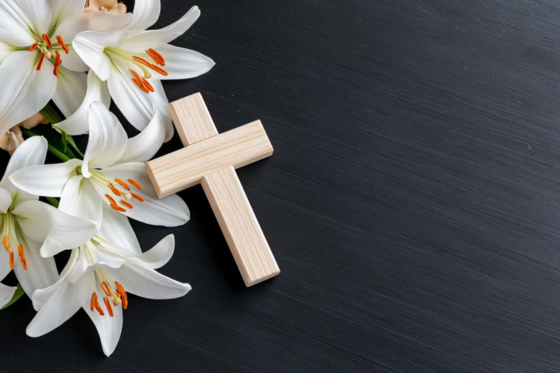 Wooden cross and white lilies arranged on dark surface with copyspace